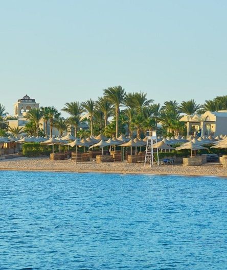 Ein Sandstrand mit zahlreichen Sonnenschirmen und Palmen vor einer Hotelanlage, aufgenommen vom blauen Meer aus. Ein Sandstrand mit zahlreichen Sonnenschirmen und Palmen vor einer Hotelanlage, aufgenommen vom blauen Meer aus.